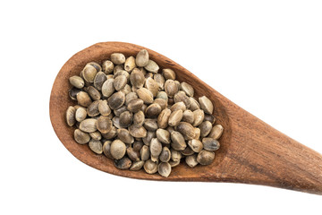 Close up of brown wooden spoon with hemp seeds from lower right corner seen directly from above and isolated on white background