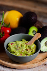 Tasty and healthy mexican snack: avocado guacamole. Homemade, served on a wooden rustic table with raw ingredients. Delicious and low calorie meal to share with friens. Close up, macro