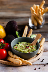 Tasty and healthy mexican snack: avocado guacamole. Homemade, served with bread stick with herbs on a wooden rustic table. Delicious and low calorie meal to share for the company. Close up, macro