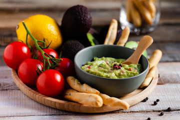Tasty and healthy mexican snack: avocado guacamole. Homemade, served with bread stick with herbs on a wooden rustic table. Delicious and low calorie meal to share for the company. Close up, macro