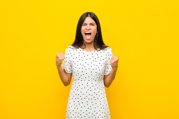 young pretty latin woman shouting aggressively with an angry expression or with fists clenched...