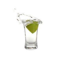 Splashing Mexican Tequila in shot glass with lime slice isolated on white