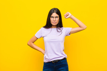young pretty latin woman feeling serious, strong and rebellious, raising fist up, protesting or...