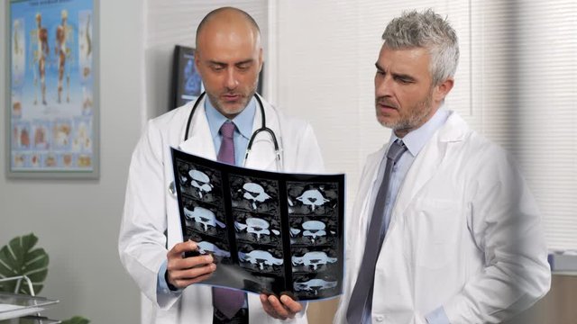 two doctors behind glass looking at x-rays having conversation about patient disease