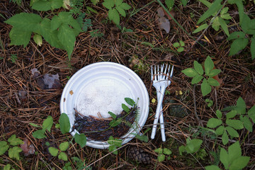 Plastic waste left in forest after a picnic. White plastic plate and two forks on the ground