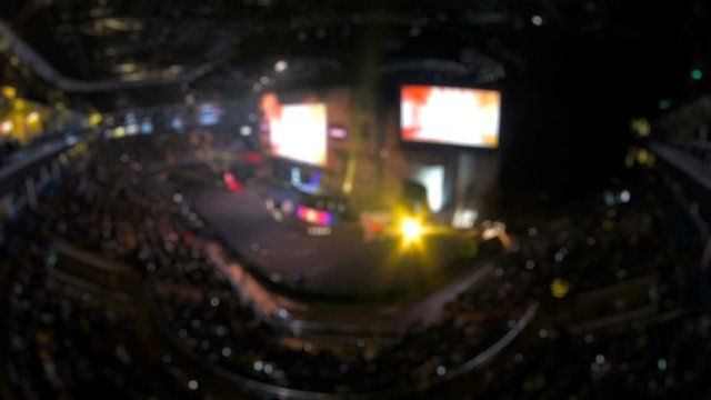 Esports event blurred backgroung. Main stage, lights, illumination, big screen with game moments from overlooking spot at the top of arena.