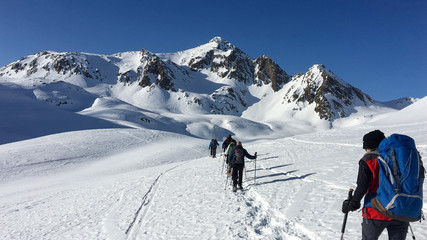 Fototapeta na wymiar In winter, some hikers walk the snowy valley at the Lucomanio pass in Switzerland.