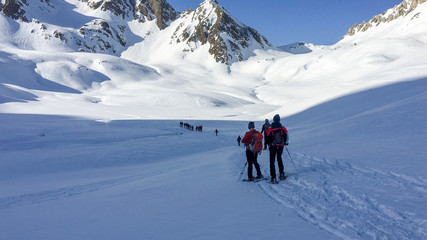 Fototapeta na wymiar In winter, some hikers walk the snowy valley at the Lucomanio pass in Switzerland.