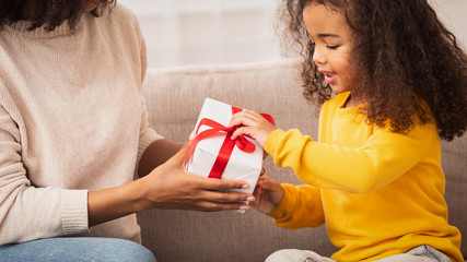 Little Girl Receiving Gift From Mother Sitting On Couch Indoor