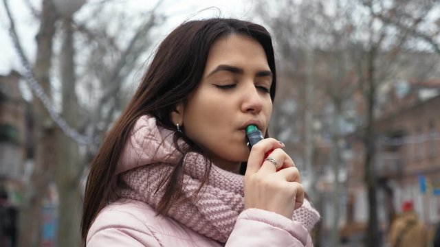 Pretty caucasian girl smoking e-cigarette on the street. Portrait of vaping person