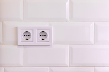 Group of two white european electrical outlets on a wall of white tile in a modern kitchen or...