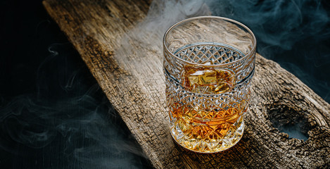 glass of whiskey with ice on a wooden table surrounded by smoke