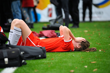 Girl football player cries lying on a soccer field during match