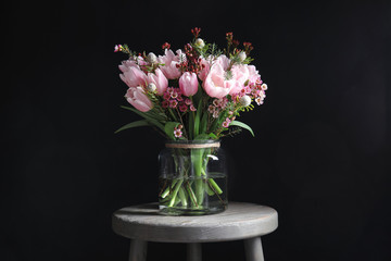 Fototapeta premium Beautiful bouquet with spring pink tulips on wooden table against black background