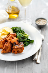 fried meat with potato chips and greens on white plate on ceramic background
