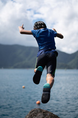 a boy jumping near lake near hill 