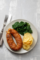 fried smoked sausage with potato chips and greens on white plate on ceramic background
