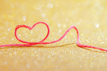 Red thread in the shape of a symbol of love of heart on a gold background for Valentine's day