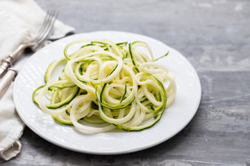 Spiral zucchini noodles on white plate on ceramic background
