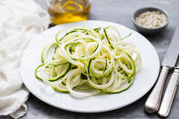 Spiral zucchini noodles on white plate on ceramic background