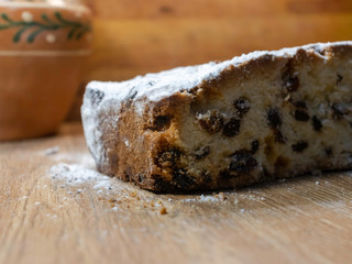 Tasty, delicious pie with raisins, sprinkled with icing sugar, cut on a wooden table. Cupcakes for holidays, dough products. With clay vintage pot in the background