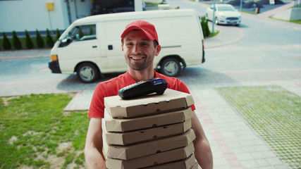 Happy pizza corrier visiting house with boxes to the customer. Convenient fast food home delivery services. Portrait of cheerful young deliveryman holding boxes with hot pizza standing by door.