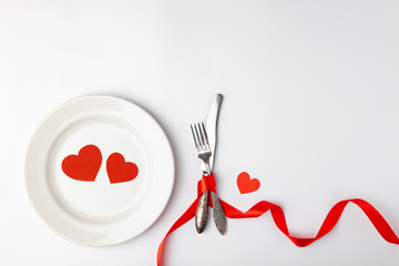 Romantic table setting on white background. Valentines day card template. Red ribbon, plate, silverware, vintage fork, hearts, knife. Concept anniversary, birthday, place for text, copyspace topview.