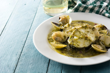 Hake fish and clams with green sauce on blue wooden table.Copy space