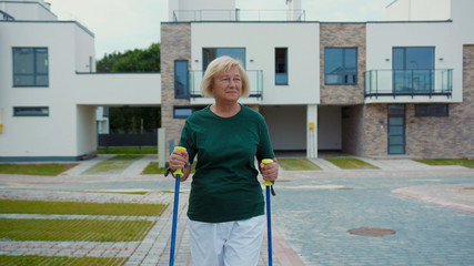 Beautiful old sportive woman in sportswear walking training with ski poles in the street. Portrait of healthy senior woman doing cardio in the morning to stay fit. Healthy lifestyle.