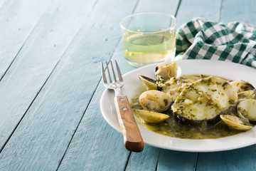 Hake fish and clams with green sauce on blue wooden table. Copy space