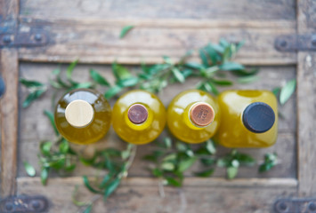 from above four bottles filled with a yellow golden liquid that looks like olive oil or a juice sorted on a wooden rustic piece of furniture in a kitchen in italy.