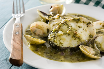 Hake fish and clams with green sauce on blue wooden table.Close up