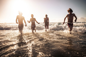 Young friends people run in the sea water together having fun in a sunny day of summer vacation -...