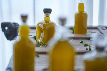 glass bottles filled with a golden liquid oil juice healthy organic vegan on a rustic wooden piece of furniture olive leaves around them in a mediterranean house sharp unsharp wellness