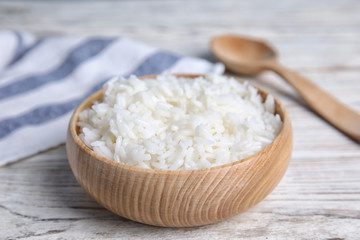 Bowl with tasty cooked rice on white wooden table, closeup