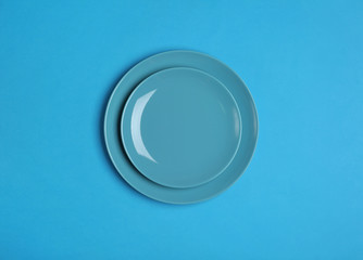 Clean empty plates on blue background, top view