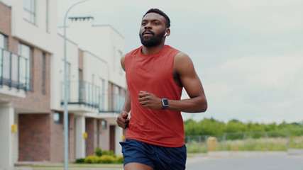 Active male runner in red sportswear and earphones jogging in the street. Outdoor portrait handsome...