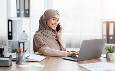 Young Arabic Businesswoman Talking On Cellphone And Using Laptop In Office