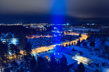 Fototapeta na wymiar Light for Independence Day of Finland, Joensuu. A ray of blue color to the sky. Aerial view of the night city.