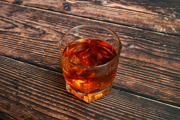 Alcohol in a glass goblet on a wooden background, cognac, whiskey, brandy with ice.
