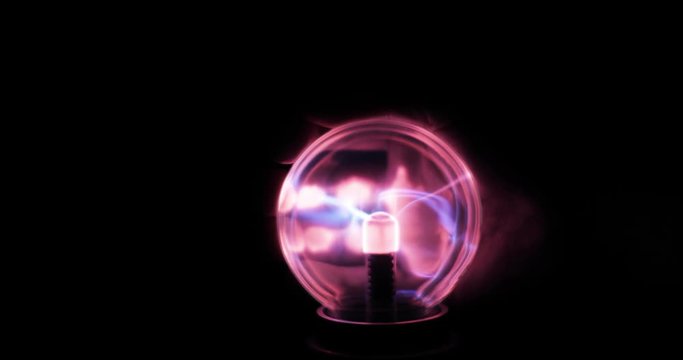 Electricity or plasma crackling. Man's hand touching tesla plasma ball with pink and blue lightnings in dark on black background, closeup view. Tesla coil experiment with electricity, glowing lamp.