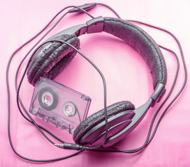 Old headphones and cassette tapes on a pink background. Outdated technology.