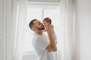 Happy Caucasian father kissing newborn baby. Male man parent holding rocking child daughter son in his hands. Authentic lifestyle candid moment. Young bearded dad family life concept.