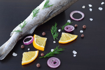 Fresh sea fish with herbs, spices and lemon on a black background.
