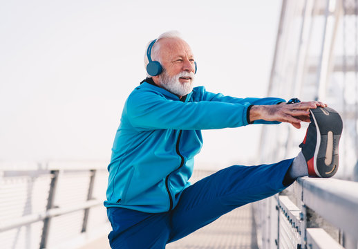 A Senior Sportsperson Stretching His Legs On A Bridge Walkway.