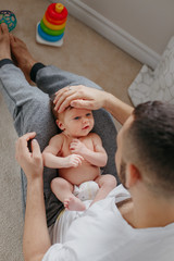 Obraz na płótnie Canvas Happy Caucasian father holding newborn baby on laps knees. Man parent embracing rocking child daughter son. Authentic lifestyle candid moment. Proud young dad. Family fathers day holiday.