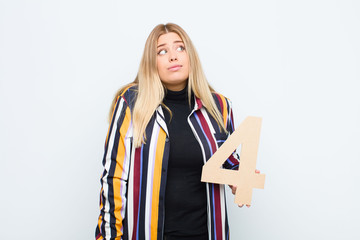 young pretty blonde woman confused, doubtful, thinking, holding a number 4.