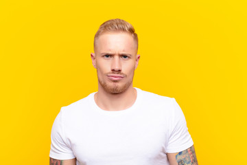 young blonde handsome man feeling confused and doubtful, wondering or trying to choose or make a...