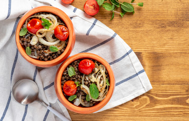 Cooked green lentils with tomatoes, onions and mint in pots on a wooden background, top view. Vegan and vegetarian food, Mediterranean cuisine.