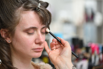 Makeup artist does makeup on the eyes of a young woman, a brush near the eye, close-up.